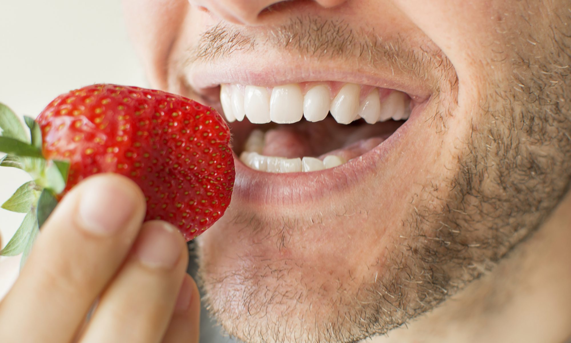 A man eating a strawberry to show the importance of maintaining a proper diet for oral health